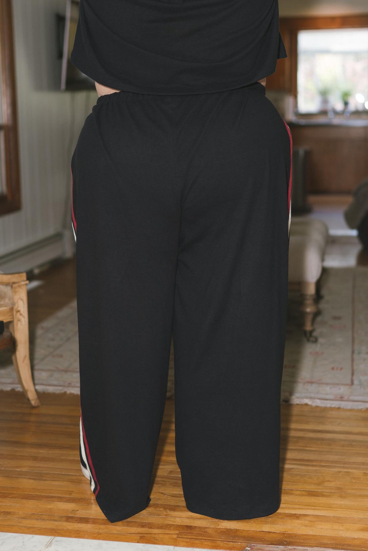 Black wide-leg sweatpants with red and white side stripes, shown on a person standing in a living room.